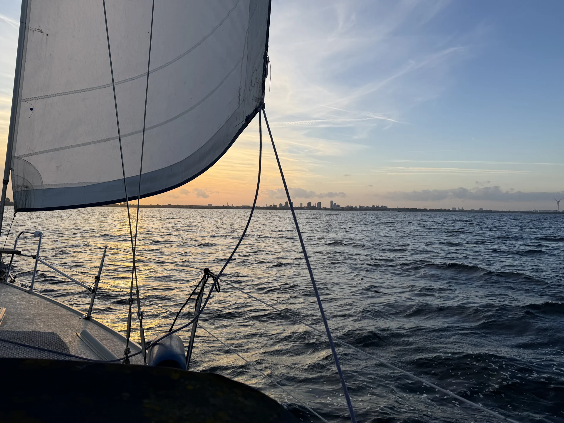 Sail and deck of a sailing boat with evening sunlight over the water.