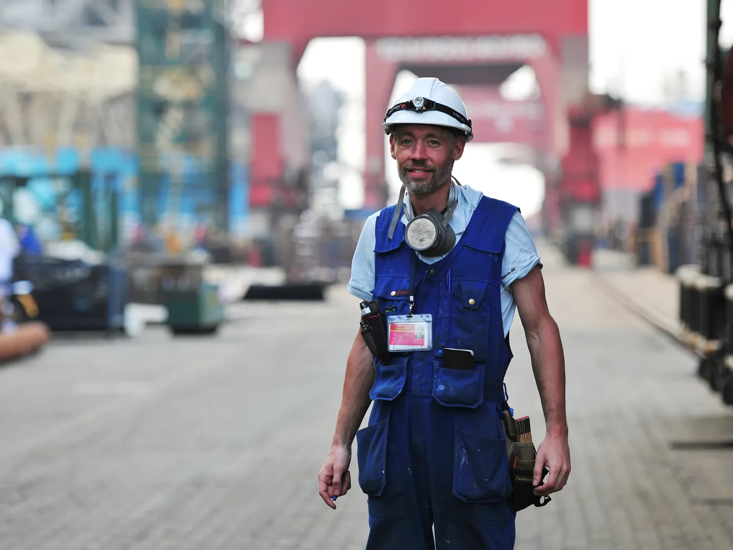 Konsulent med hjelm og arbejdstøj på et industriområde ved havnen.